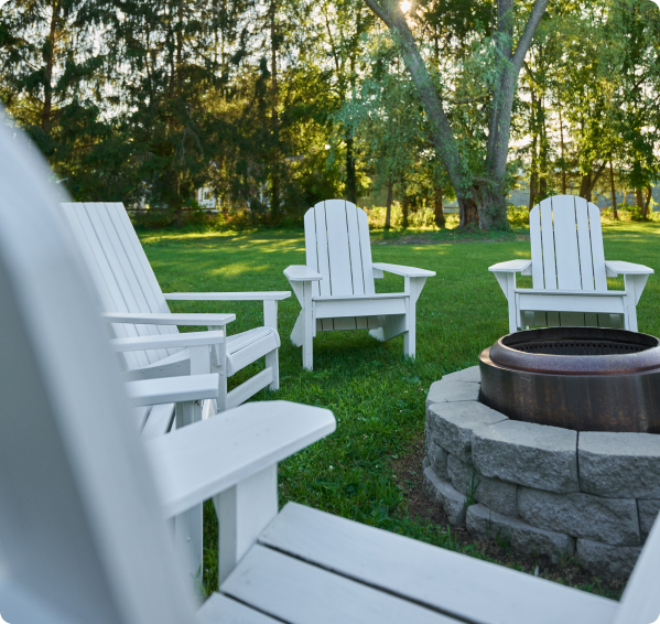 White Adirondack chairs around a stone fire pit on the inn's lawn, a guest amenity available to those staying at Pleasant Valley Inn.